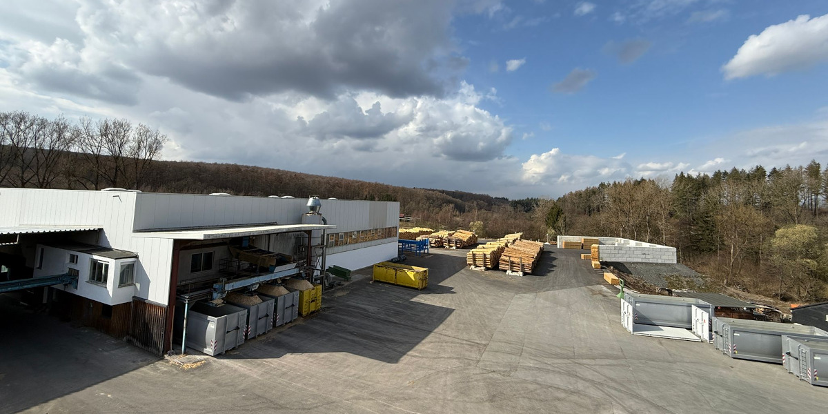 Das Sägewerk in Warstein-Hirschberg bei schönem Wetter mit Halle und Lagerplatz fotografiert.